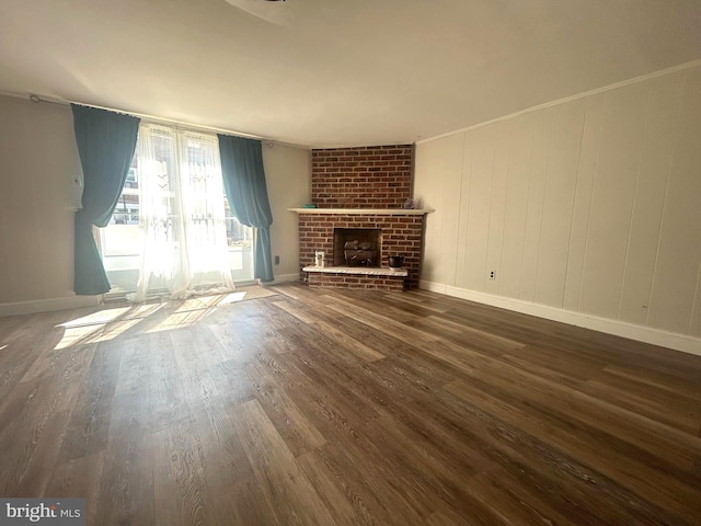 unfurnished living room featuring brick wall, a brick fireplace, crown molding, and dark hardwood / wood-style floors