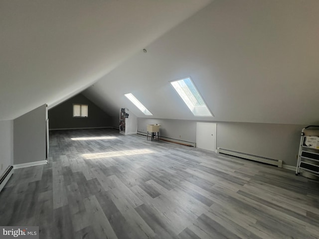 additional living space with lofted ceiling with skylight, hardwood / wood-style flooring, and a baseboard radiator