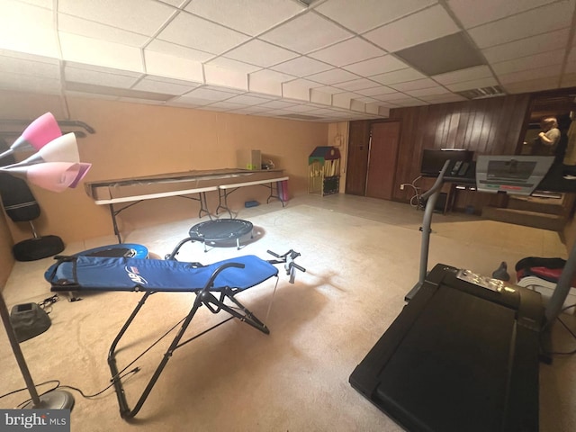 exercise room with a paneled ceiling and wood walls