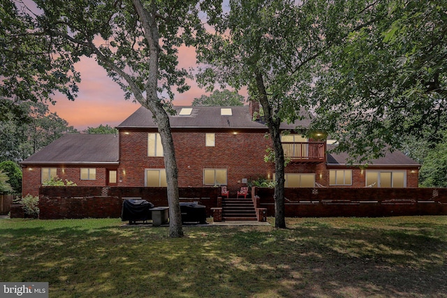 back house at dusk featuring a balcony and a yard