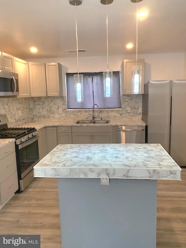 kitchen with tasteful backsplash, hanging light fixtures, light wood-type flooring, sink, and appliances with stainless steel finishes