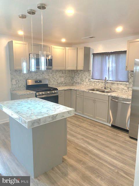 kitchen with hanging light fixtures, light hardwood / wood-style flooring, backsplash, and stainless steel appliances