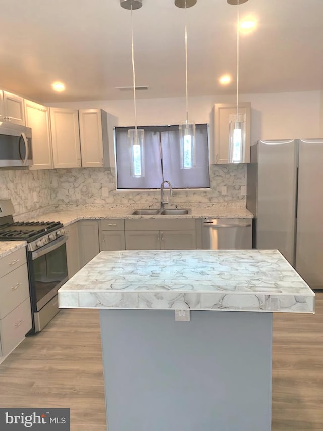 kitchen featuring stainless steel appliances, sink, hanging light fixtures, backsplash, and light wood-type flooring