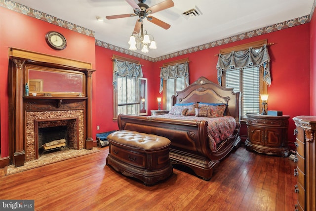 bedroom featuring a high end fireplace, hardwood / wood-style flooring, and ceiling fan