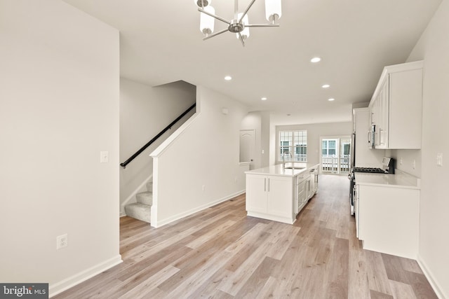 kitchen with sink, a center island with sink, light wood-type flooring, stainless steel appliances, and white cabinets