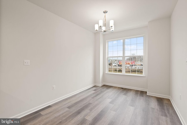 spare room with a chandelier and light wood-type flooring