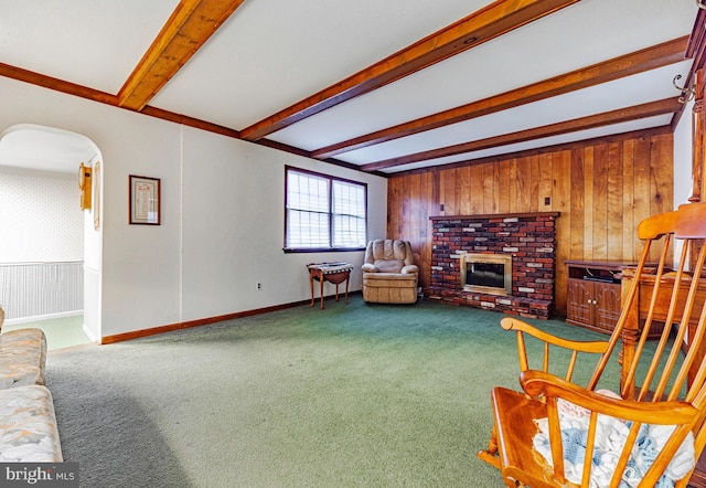 living room featuring beamed ceiling, carpet, a brick fireplace, and wood walls