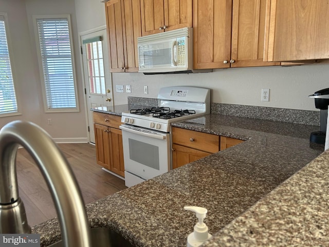 kitchen featuring dark hardwood / wood-style flooring, white appliances, dark stone counters, and sink