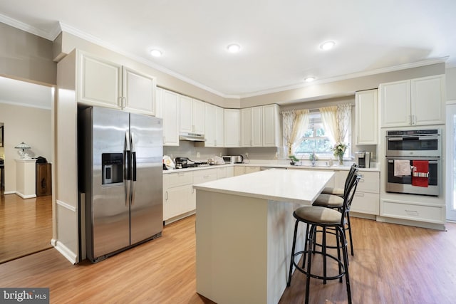 kitchen with a center island, stainless steel appliances, a breakfast bar area, white cabinets, and light wood-type flooring