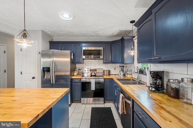 kitchen with pendant lighting, butcher block counters, stainless steel appliances, blue cabinetry, and sink