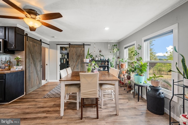 dining room with ceiling fan, crown molding, a barn door, and light hardwood / wood-style flooring