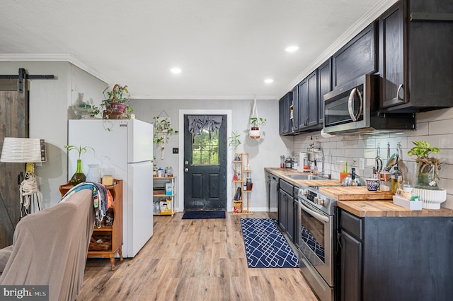 kitchen featuring a barn door, appliances with stainless steel finishes, crown molding, and butcher block countertops