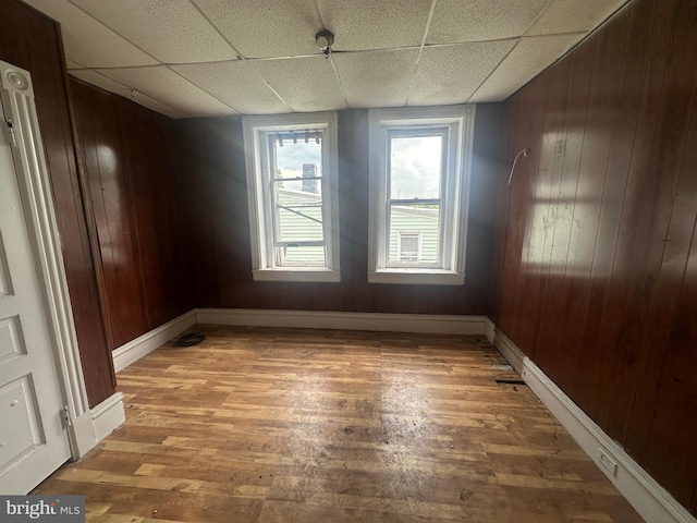 spare room featuring a paneled ceiling, wood walls, and wood-type flooring