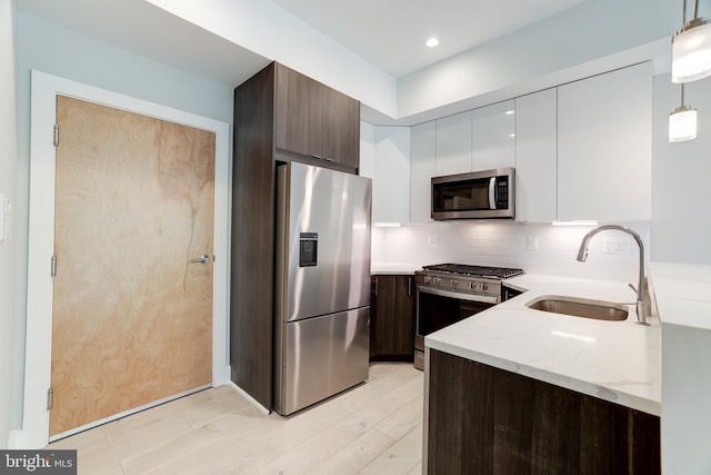 kitchen with appliances with stainless steel finishes, dark brown cabinets, hanging light fixtures, white cabinets, and sink