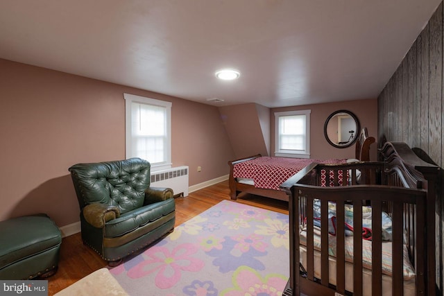 bedroom featuring radiator, wood walls, a nursery area, and light wood-type flooring