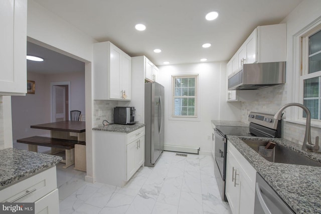 kitchen featuring backsplash, range hood, white cabinetry, stainless steel appliances, and dark stone counters