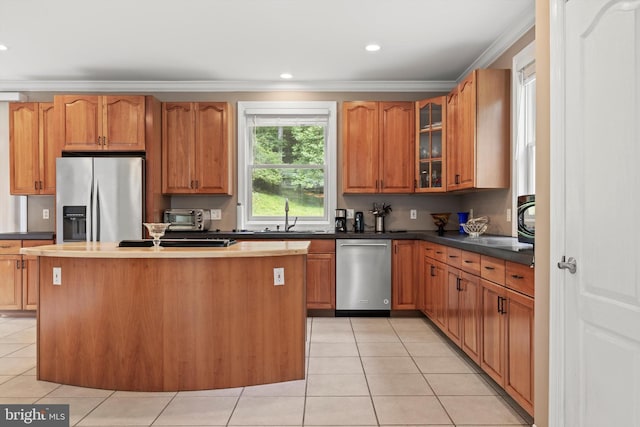 kitchen with appliances with stainless steel finishes, ornamental molding, sink, light tile patterned floors, and a center island