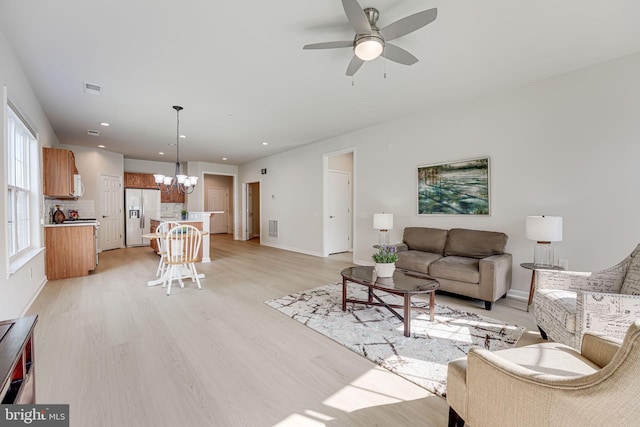 living room featuring ceiling fan with notable chandelier and light wood-type flooring