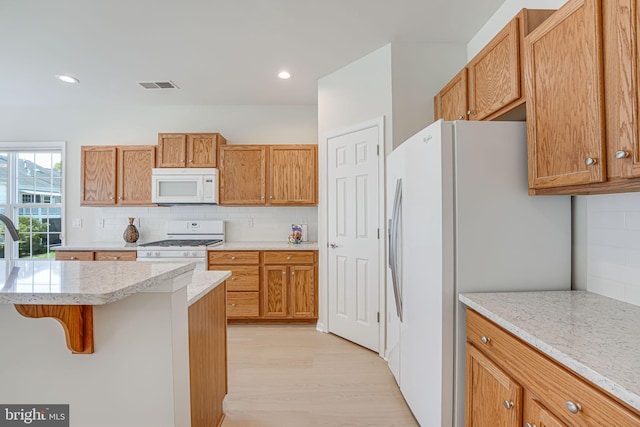 kitchen featuring a kitchen breakfast bar, decorative backsplash, light hardwood / wood-style flooring, and white appliances