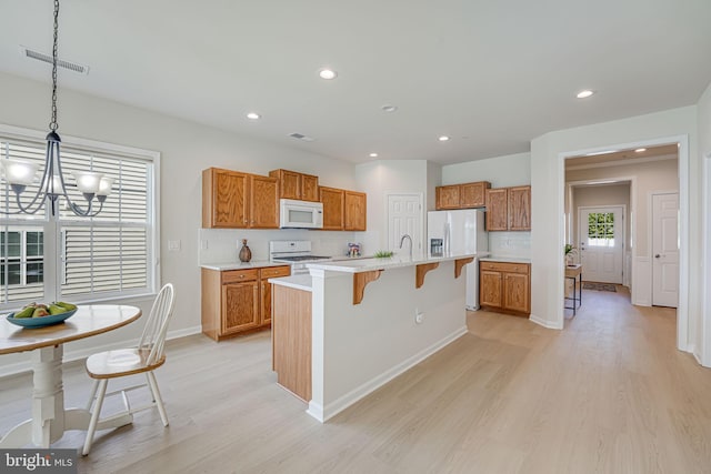 kitchen featuring light wood-type flooring, a breakfast bar, white appliances, hanging light fixtures, and an island with sink