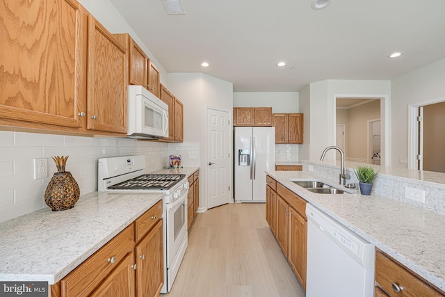 kitchen featuring light wood-type flooring, backsplash, light stone counters, white appliances, and sink