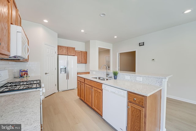 kitchen with decorative backsplash, white appliances, sink, a center island with sink, and light hardwood / wood-style floors