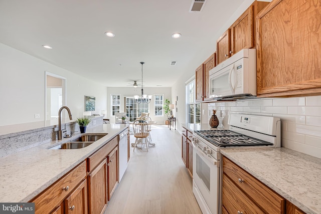 kitchen featuring light wood-type flooring, light stone counters, white appliances, sink, and a chandelier