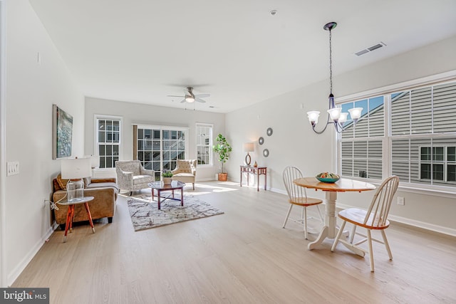 dining space with ceiling fan with notable chandelier and light hardwood / wood-style floors