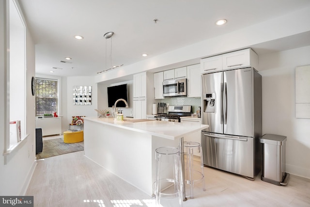 kitchen with a kitchen bar, stainless steel appliances, a kitchen island with sink, light hardwood / wood-style floors, and white cabinetry