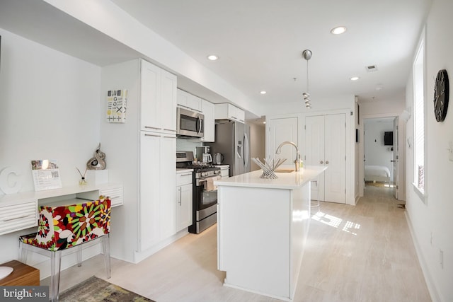 kitchen featuring sink, light hardwood / wood-style flooring, pendant lighting, white cabinets, and appliances with stainless steel finishes