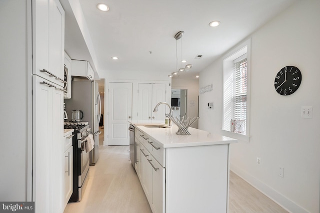 kitchen with sink, light hardwood / wood-style flooring, a kitchen island with sink, white cabinets, and appliances with stainless steel finishes