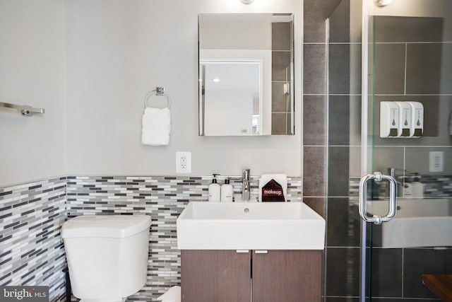 bathroom featuring vanity, toilet, a shower with shower door, and tile walls