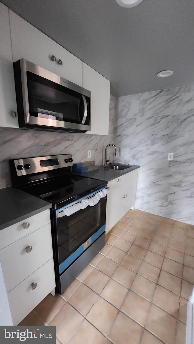 kitchen featuring tasteful backsplash, stainless steel appliances, white cabinets, sink, and light tile patterned flooring