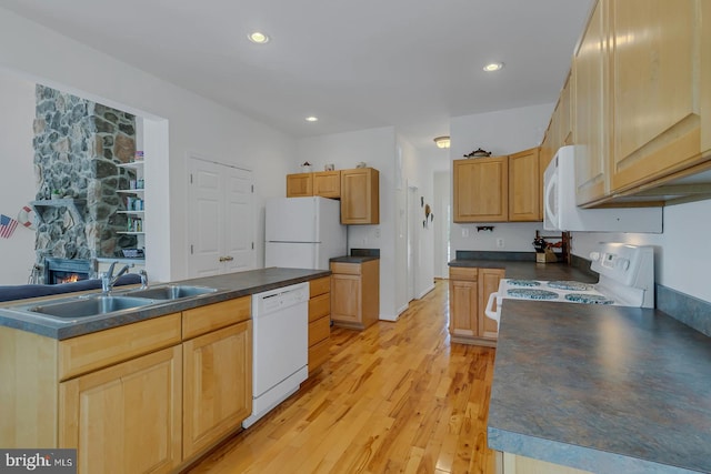 kitchen featuring light hardwood / wood-style flooring, white appliances, a kitchen island, a stone fireplace, and sink