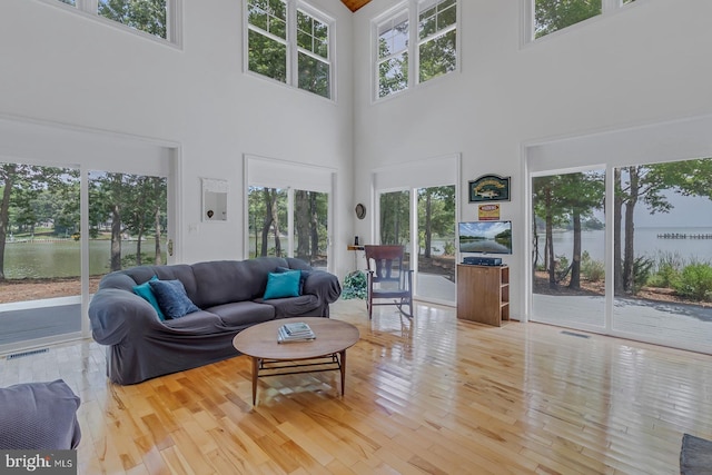 living room with a water view, light wood-type flooring, and a high ceiling