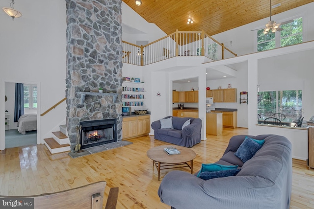 living room with wood ceiling, ceiling fan, light hardwood / wood-style floors, a stone fireplace, and high vaulted ceiling