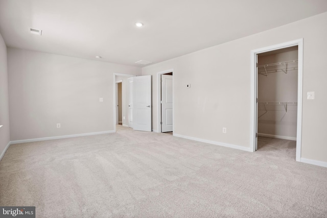 unfurnished bedroom featuring a walk in closet, light colored carpet, and a closet