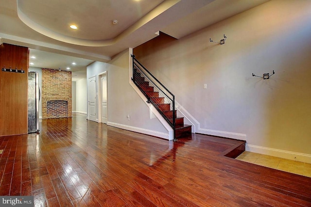 interior space with wood-type flooring, a tray ceiling, and a brick fireplace