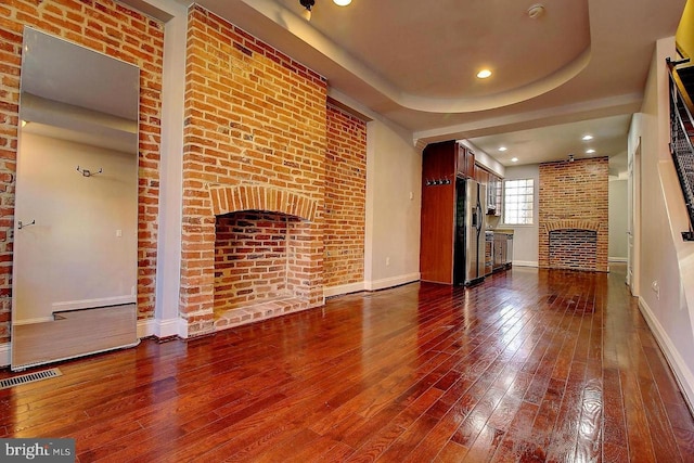 unfurnished living room with a fireplace, wood-type flooring, a tray ceiling, and brick wall