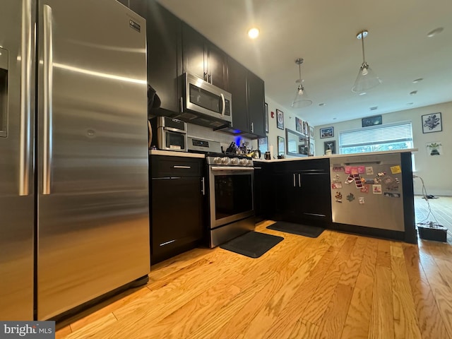 kitchen with appliances with stainless steel finishes, hanging light fixtures, and light hardwood / wood-style floors