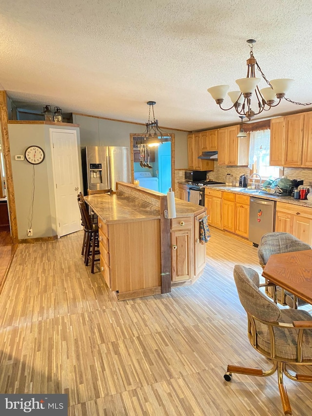 kitchen featuring stainless steel appliances, a notable chandelier, decorative light fixtures, decorative backsplash, and a kitchen island