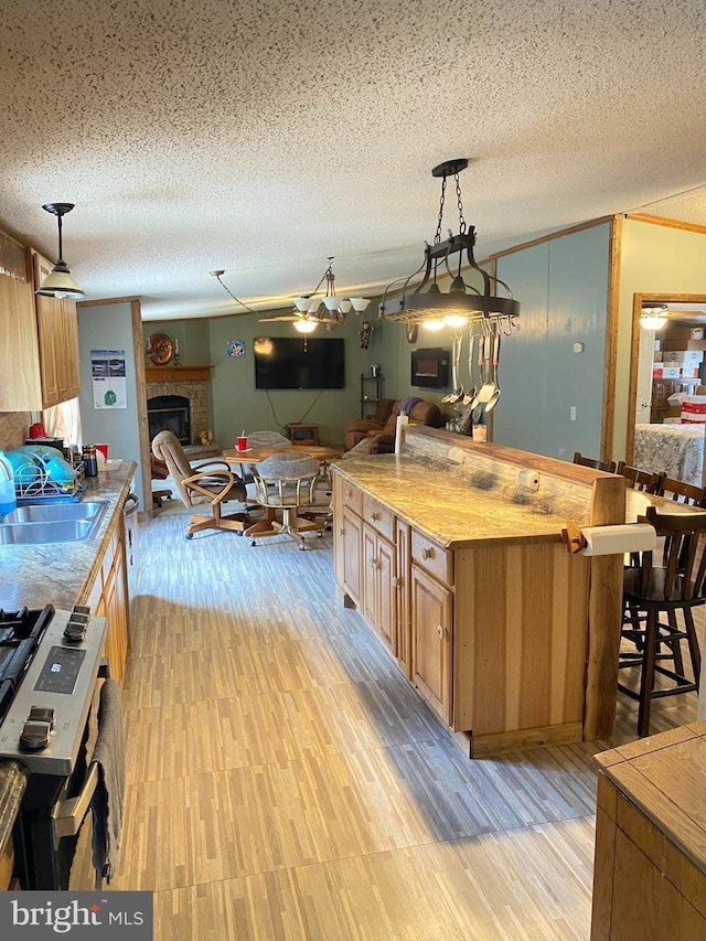 kitchen with a kitchen breakfast bar, stove, sink, a center island with sink, and hanging light fixtures