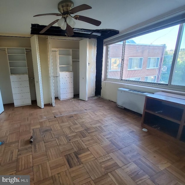 unfurnished bedroom with ceiling fan, light parquet floors, and two closets