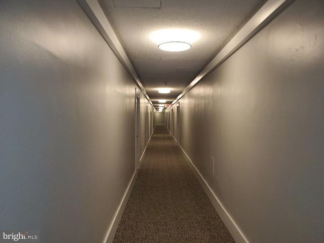 hallway featuring dark colored carpet and a textured ceiling