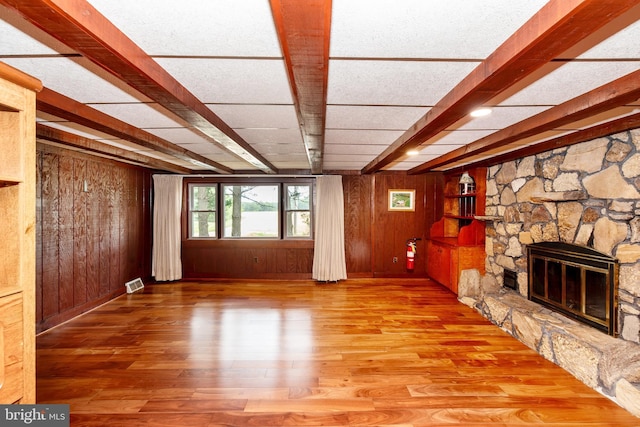 unfurnished living room with a fireplace, wooden walls, beamed ceiling, and wood-type flooring