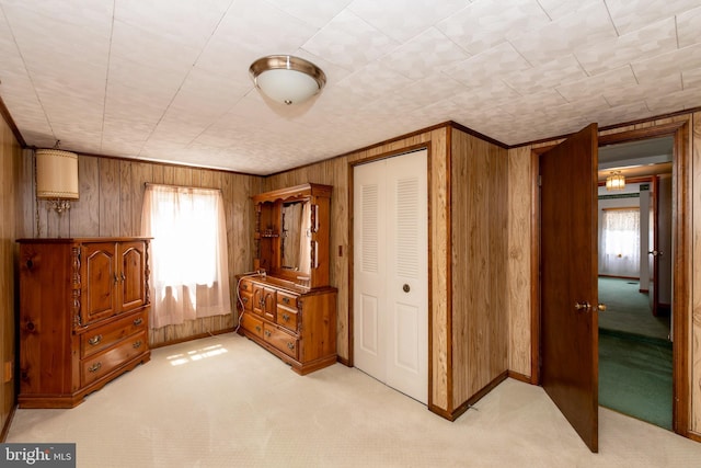 bedroom with multiple windows, light colored carpet, a closet, and wood walls