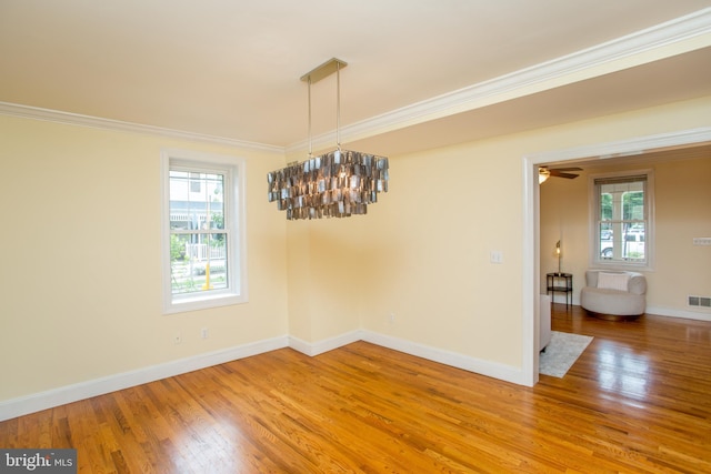 unfurnished dining area featuring ceiling fan with notable chandelier, crown molding, and hardwood / wood-style flooring