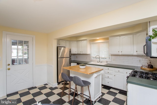 kitchen featuring a kitchen island, sink, stainless steel refrigerator, white cabinetry, and butcher block counters