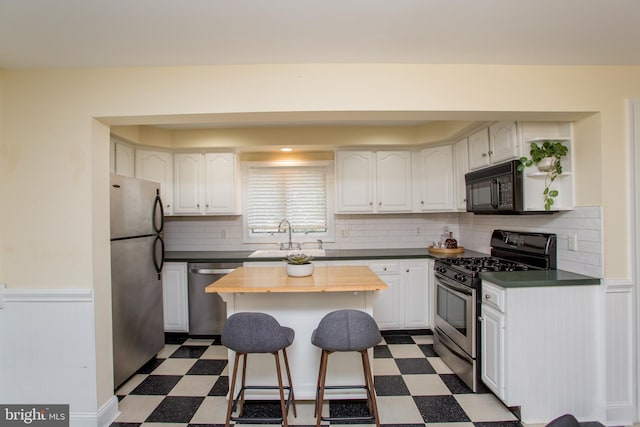 kitchen featuring wooden counters, white cabinetry, stainless steel appliances, sink, and a breakfast bar