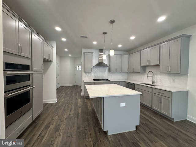 kitchen featuring wall chimney exhaust hood, black gas stovetop, a kitchen island, sink, and hanging light fixtures